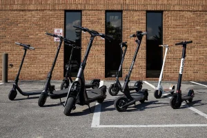 A variety of electric scooters parked on a paved surface during a product test