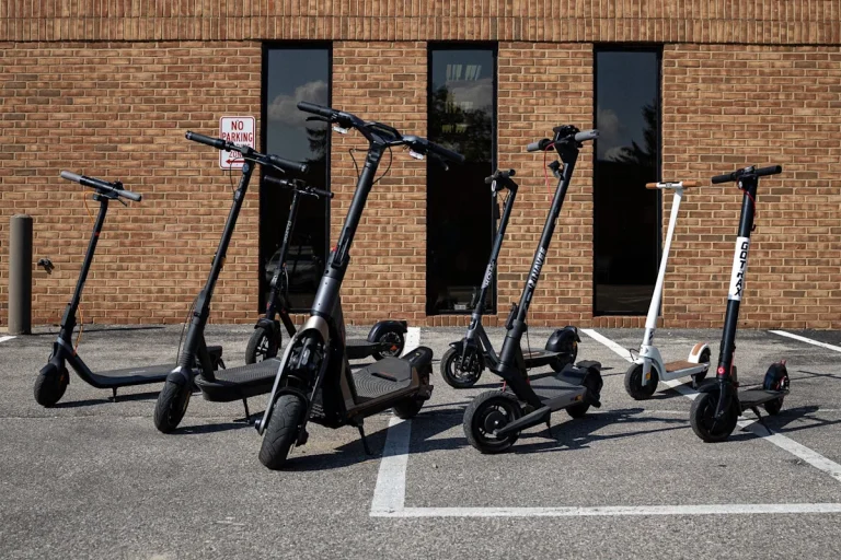 A variety of electric scooters parked on a paved surface during a product test