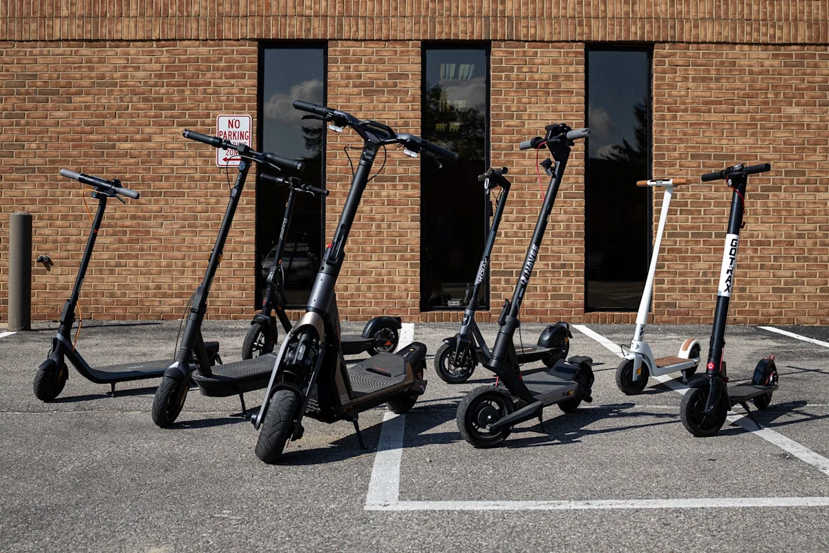 A variety of electric scooters parked on a paved surface during a product test