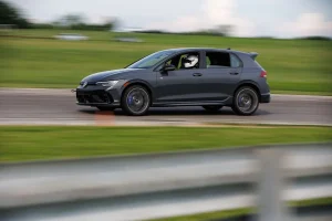 The 2026 VW Golf R parked near a racetrack showing its sleek design and forged wheels.