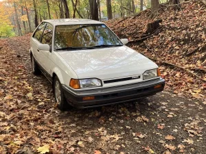 A classic white 1988 Mazda 323 GTX rally hatchback parked on a road