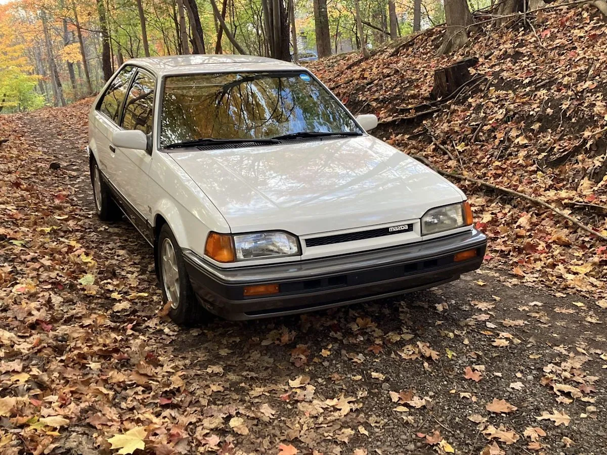 A classic white 1988 Mazda 323 GTX rally hatchback parked on a road