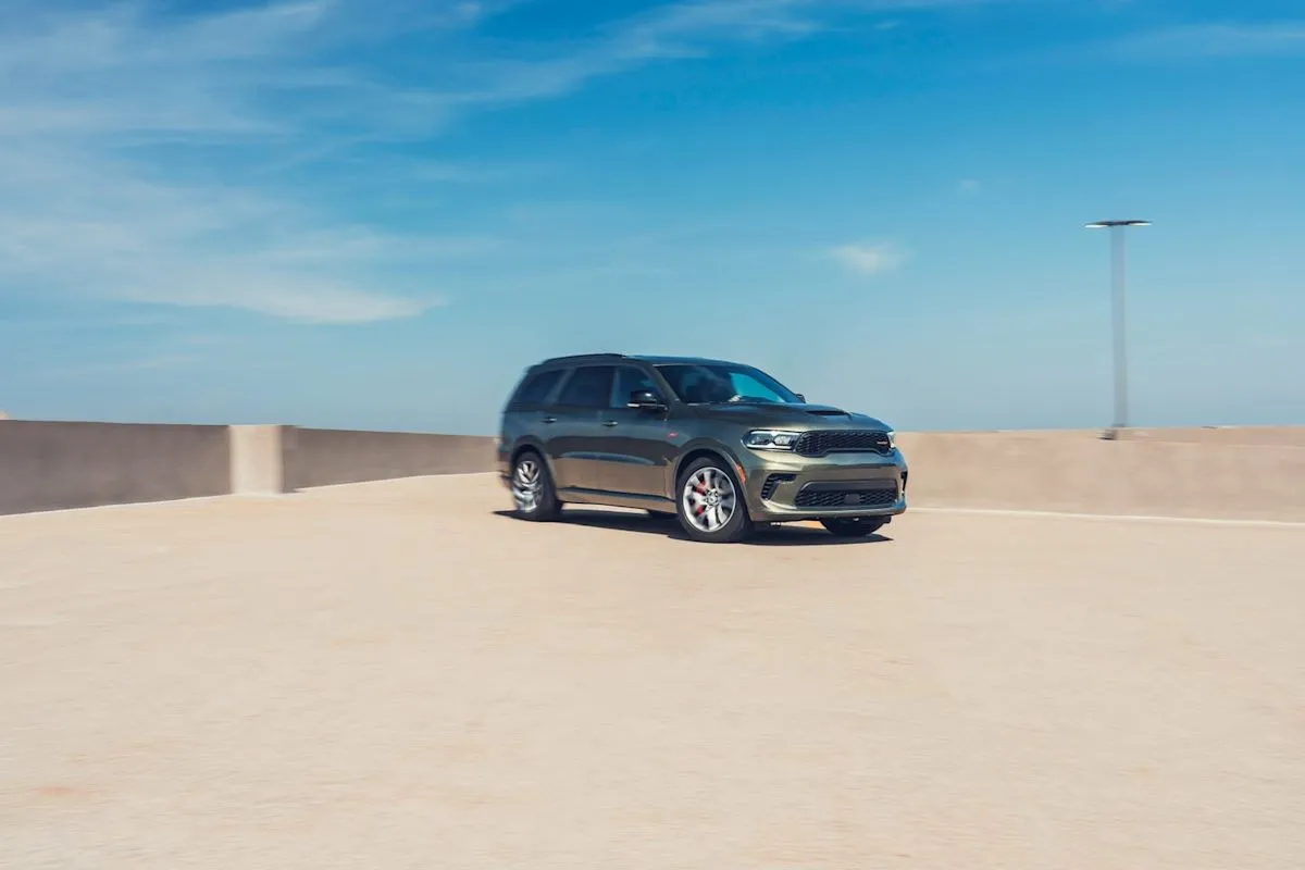 A green 2026 Dodge Durango R/T driving on an open road showcasing its muscular front hood and classic SUV design
